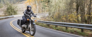 A woman wearing a helmet and protective clothing rides a motorcycle down an empty road in winter.