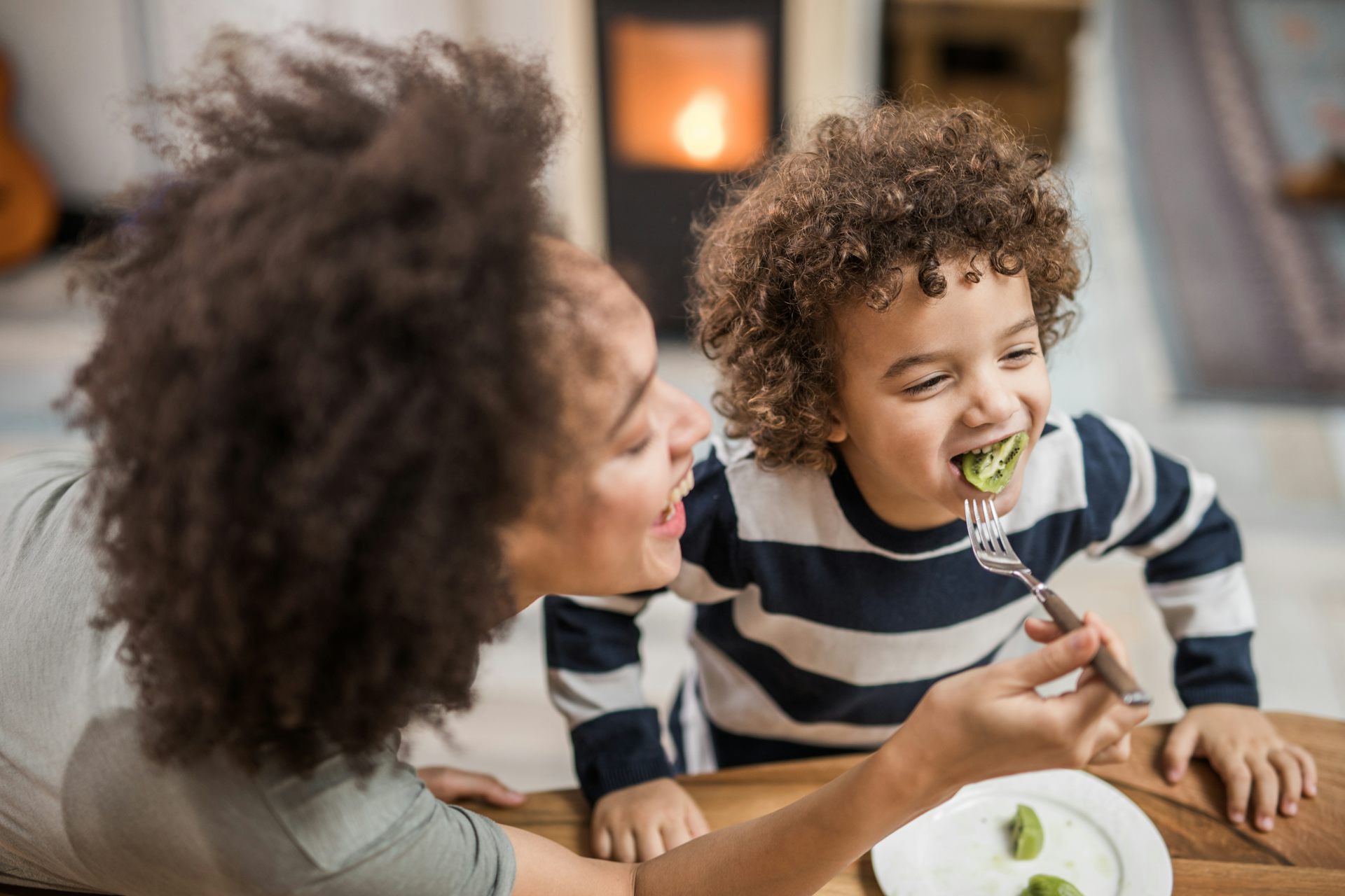 woman holding fork with kiwi in child's mouth