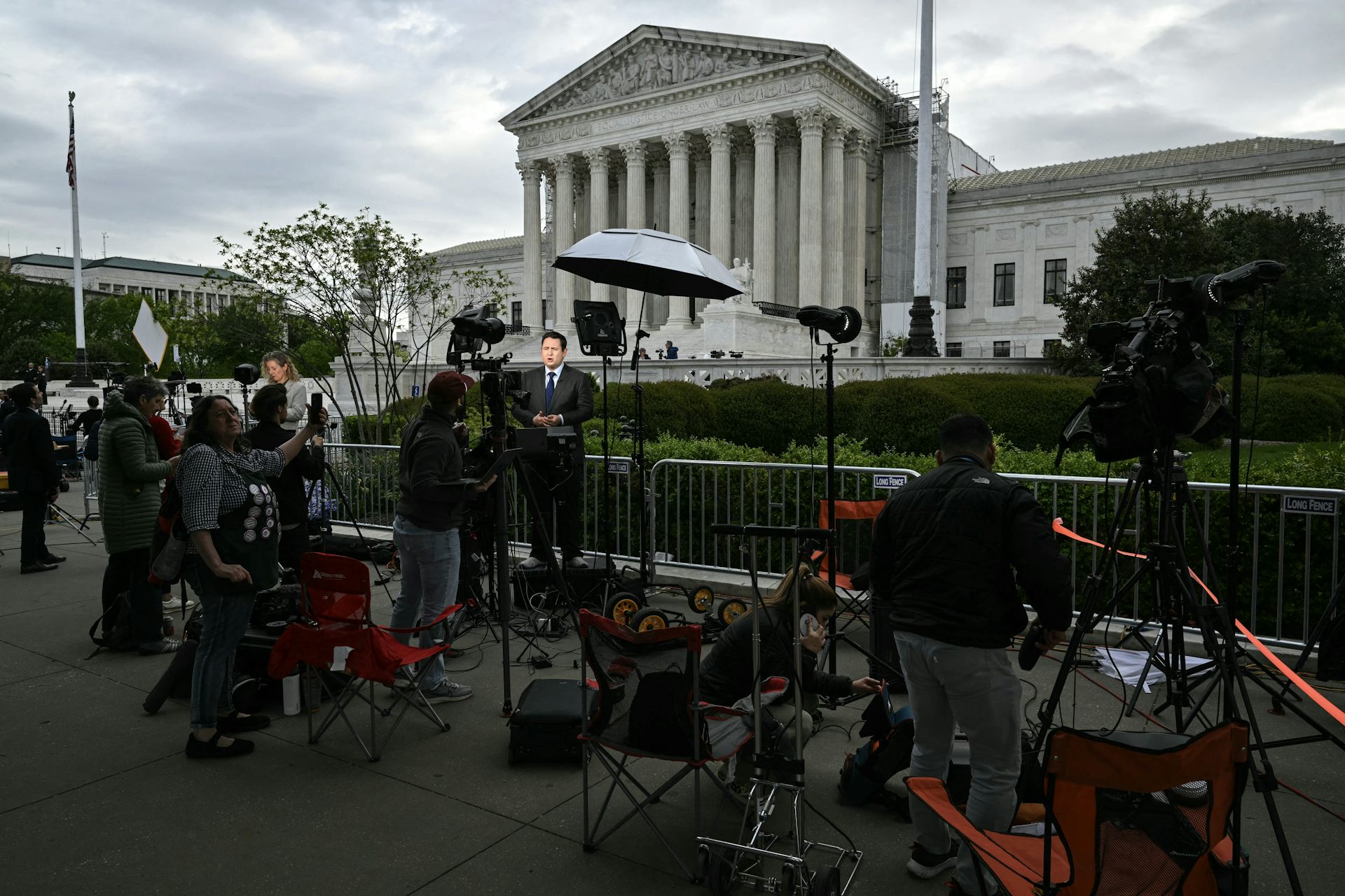 Reporters and camera operators set up in front of a large white, columned building.