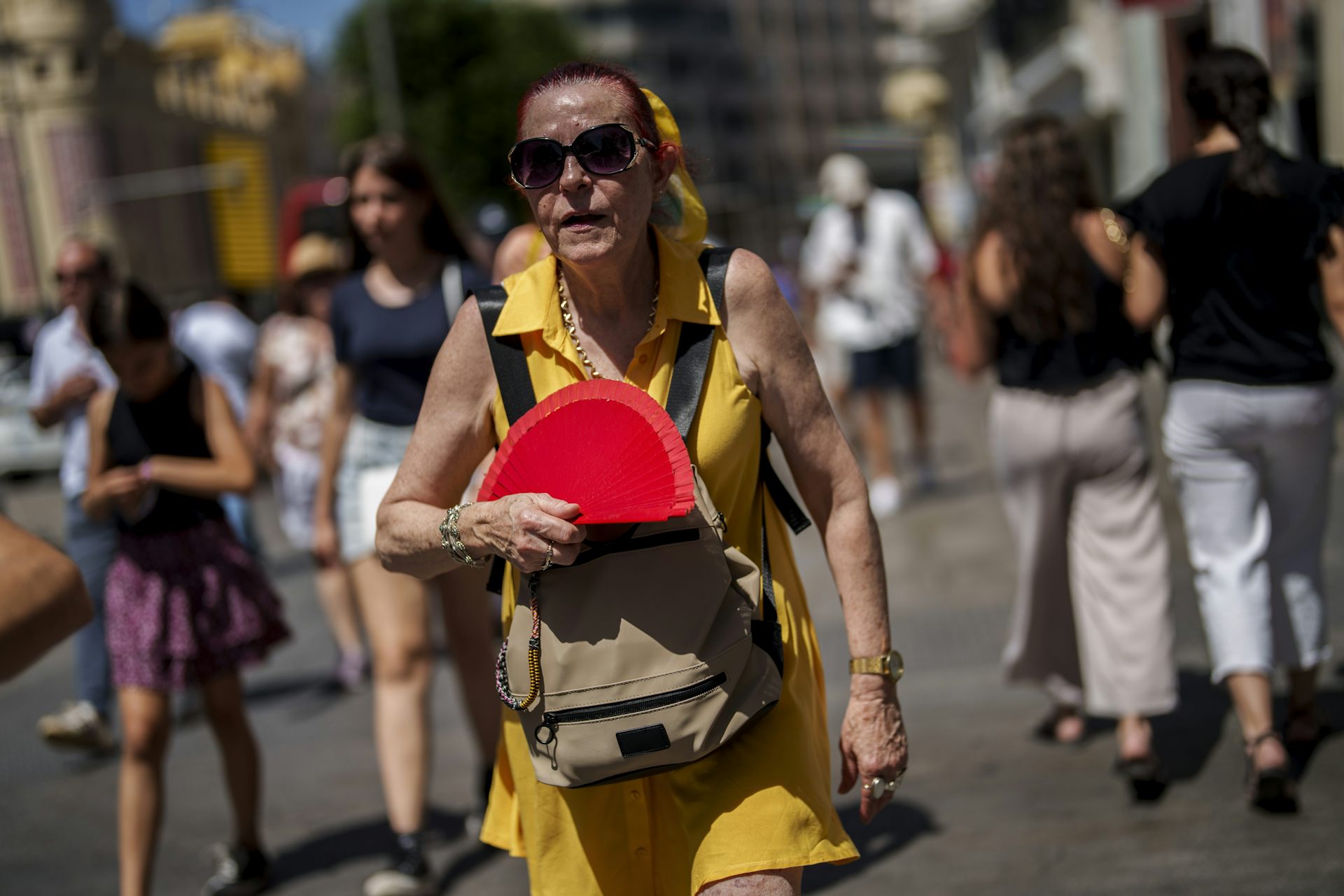 An older woman in Spain sweats as she waves a fan in the heat.