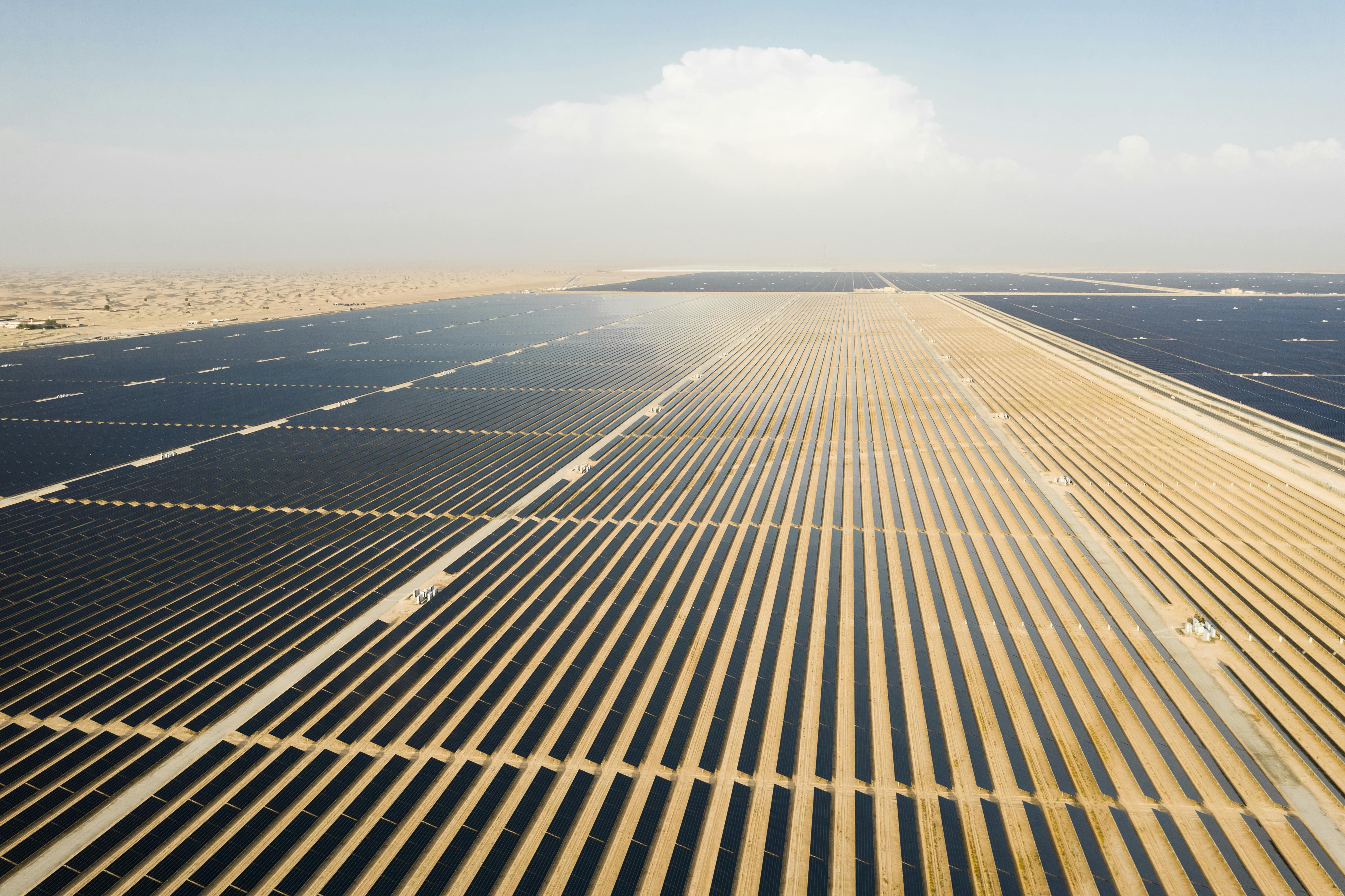Photo depicts an Aerial view of a landscape with photovoltaic solar panel farm producing sustainable renewable energy in a desert power plant.