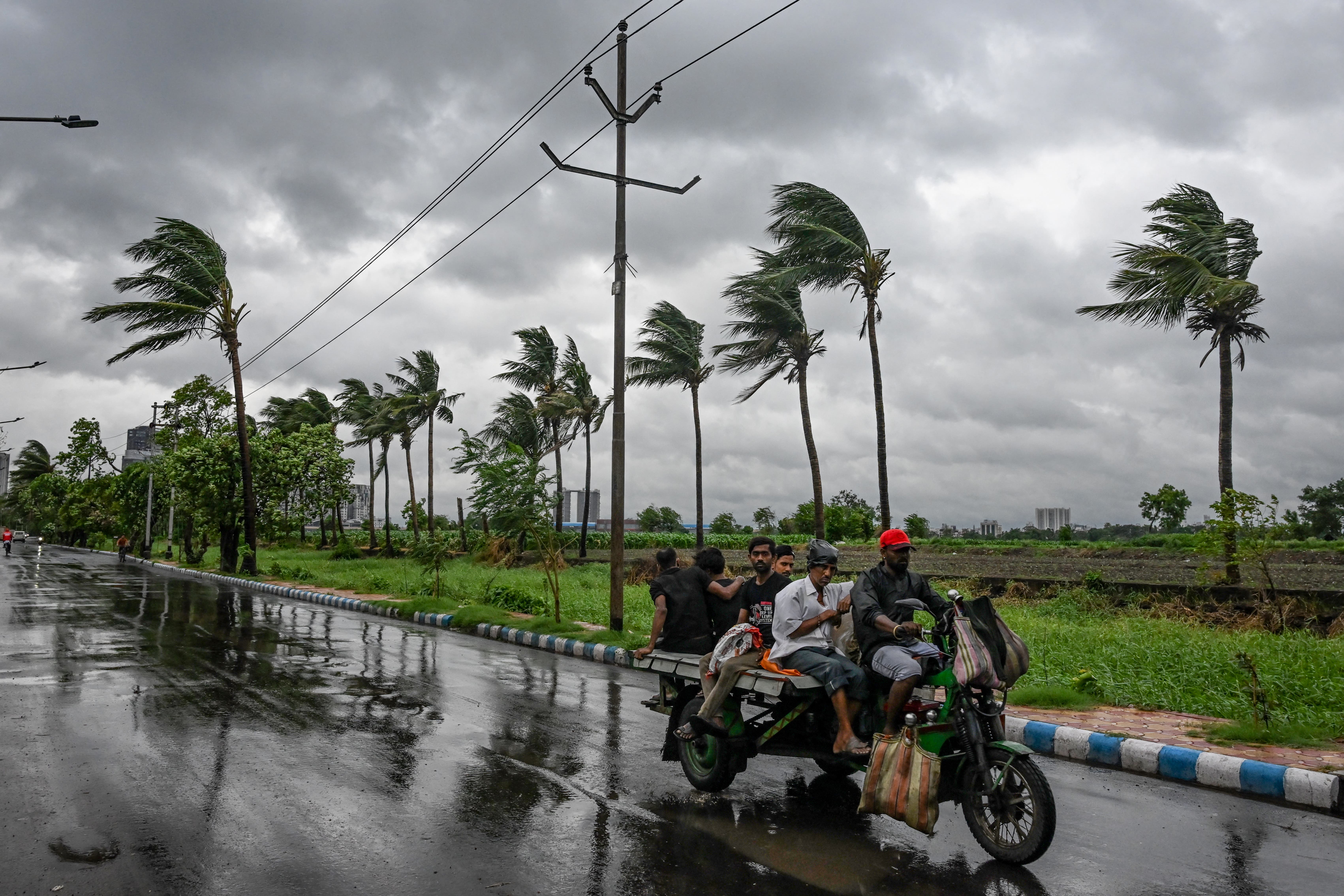 <p>Commuters travel on a motorised three-wheeler along a road as rain clouds loom over the sky, due to the effect of cyclone Remal, in Kolkata on 26 May 2024</p>