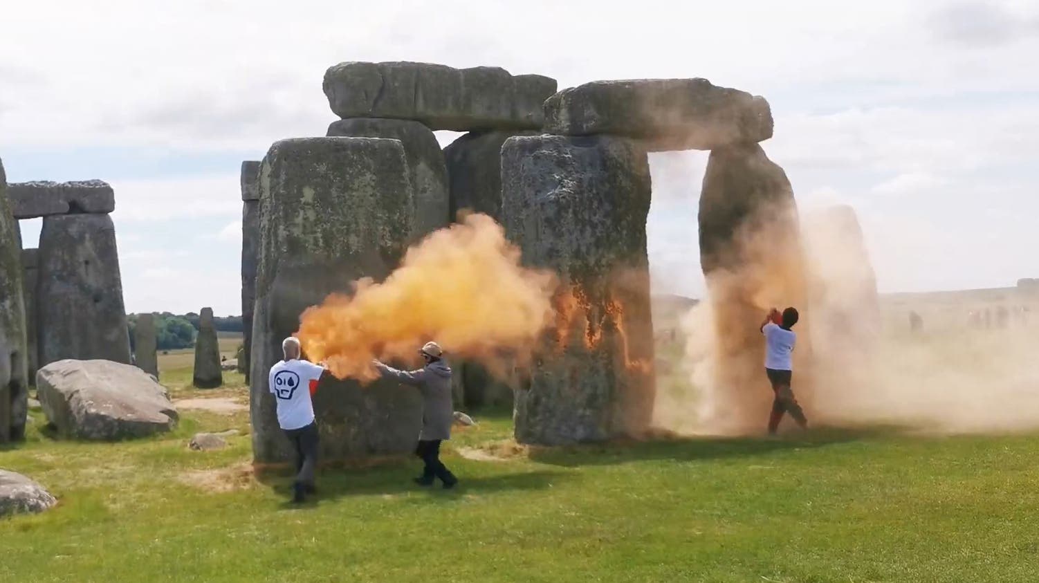 <p>Two people in Just Stop Oil T-shirts, named by the climate protest group as Rajan Naidu, 73, and Niamh Lynch, 21, spray the ancient structure with canisters of orange powder paint</p>