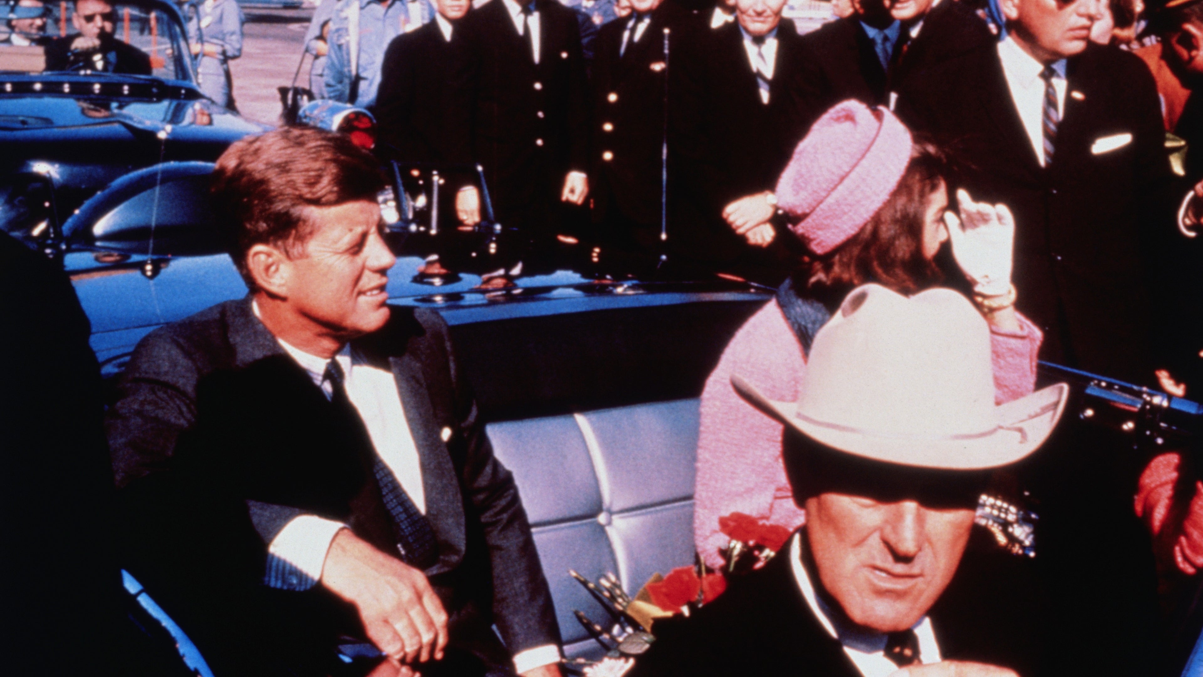 Texas Governor John Connally adjusts his tie (foreground) as President and Mrs. Kennedy, in a pink outfit, settled in rear seats, prepared for motorcade into city from airport, Nov. 22. After a few speaking stops, the President was assassinated in the same car.