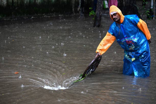 <p>File: A municipal worker standing near a manhole in a flooded street in India</p>