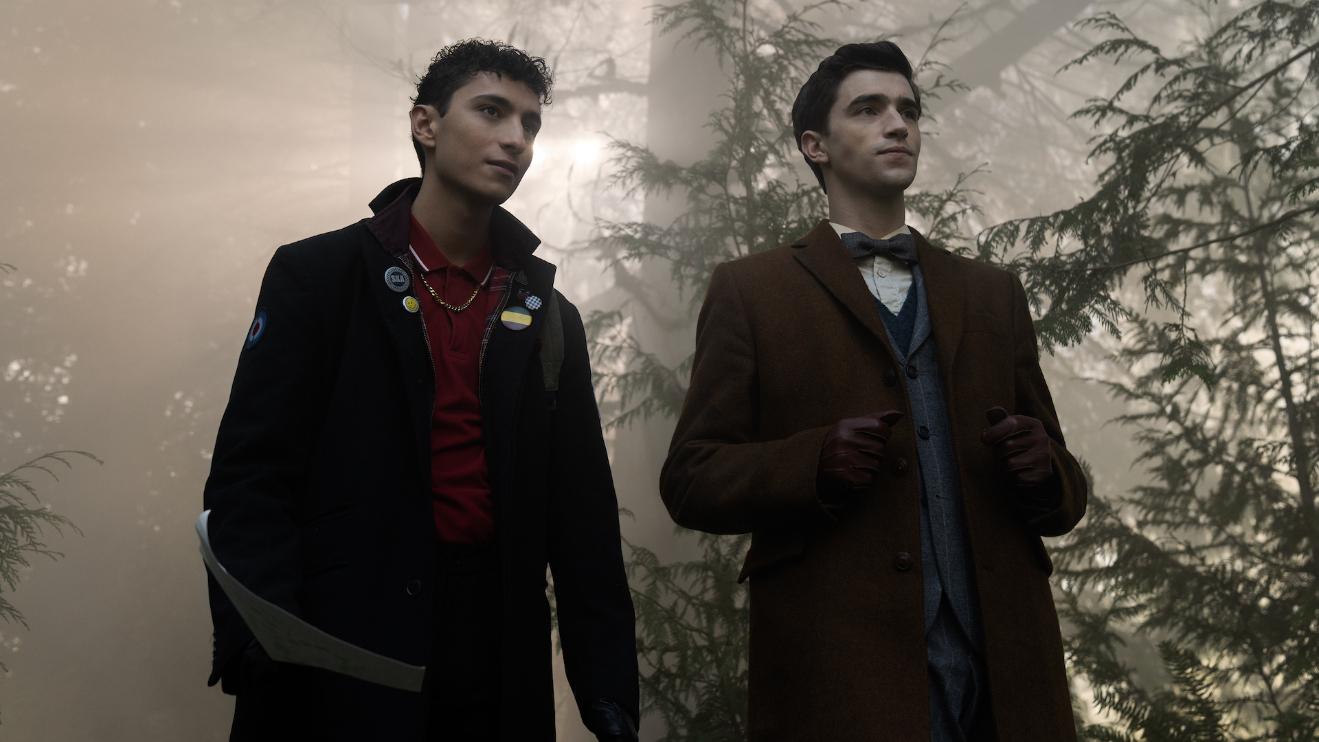Two young men in a foggy forest, one wearing a dark blazer and the other in a black jacket; still from 'Dead Boy Detectives'