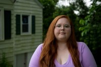 A photo of a woman posing for a portrait outside by her house.