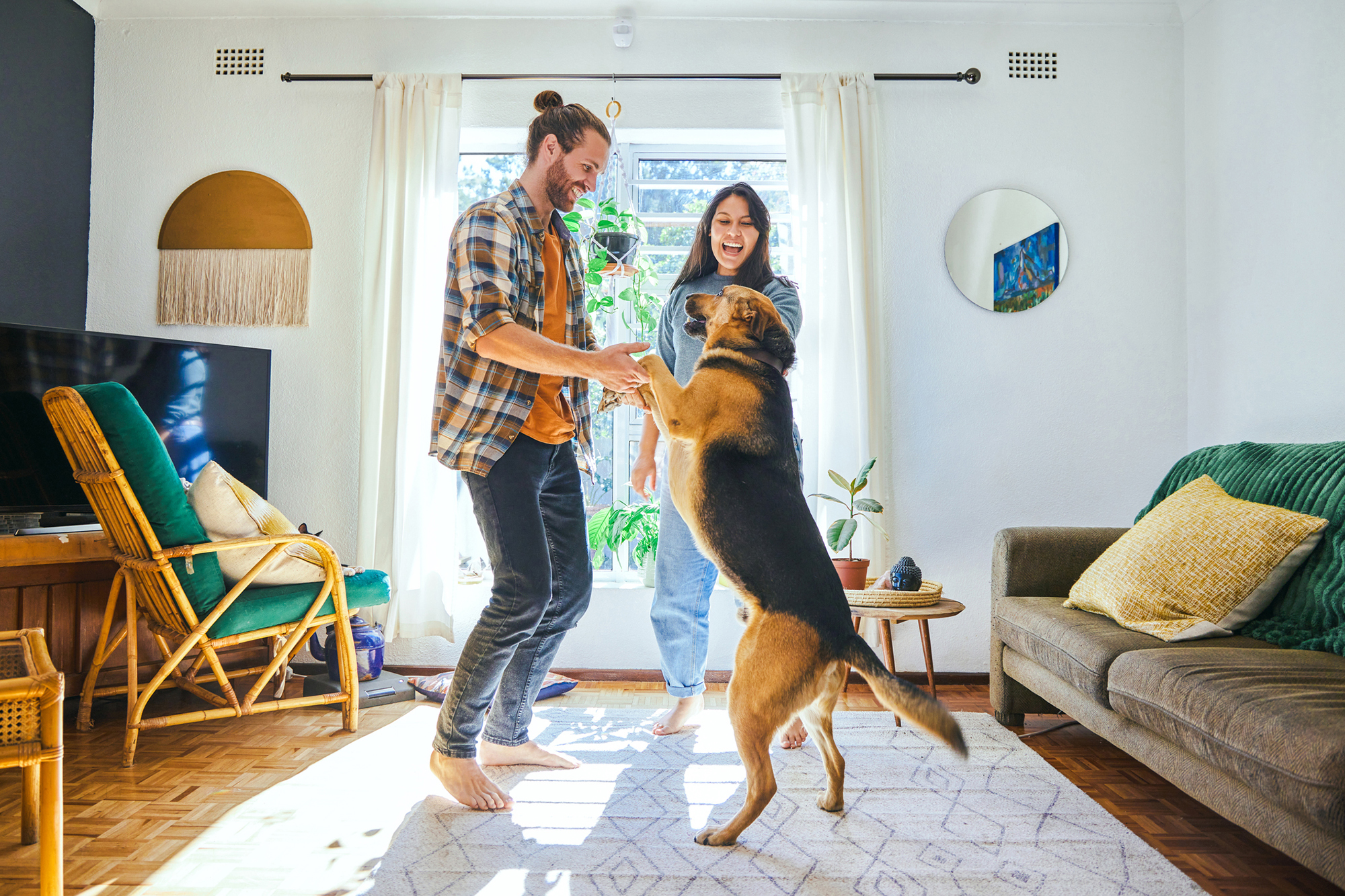A young couple playing with their dog in the house.