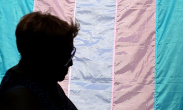 A silhouette of a person in front of a trans pride flag.