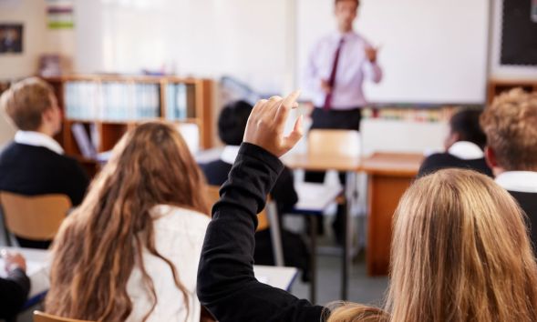 A person raising their hand in a classroom.
