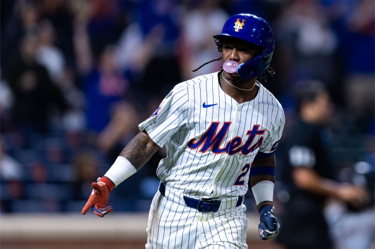 A baseball player in a uniform blowing a bubble with gum