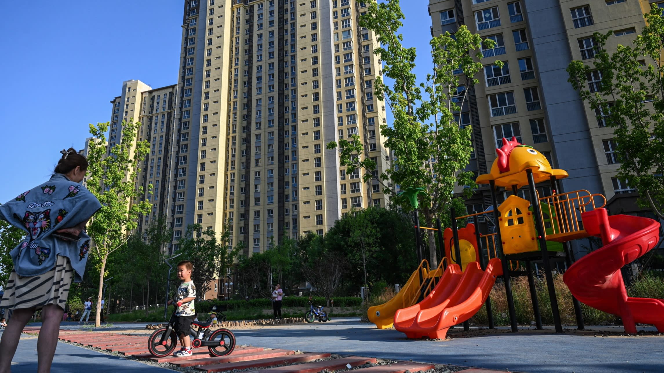 A woman watches her child at a children’s playground of a residential compound of high-rise buildings in Beijing