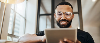 A man is wearing glasses, black tee, holding a tablet and smiling.