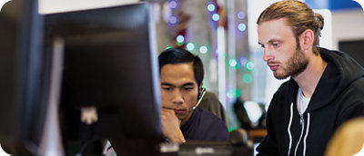Two men focused on a computer screen in a modern office setting, one asian and one caucasian