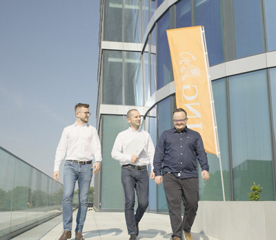 Três homens caminhando na frente de um prédio com um anúncio em faixa com o logotipo da ING.
