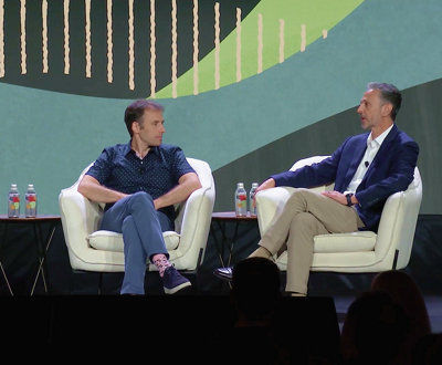 Two men sitting in chairs talking on stage.