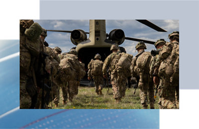 Soldiers in camouflage gear boarding a military transport aircraft in a grassy field under a cloudy sky.