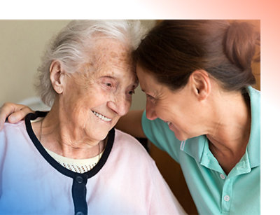 Uma mulher idosa sorridente com cabelos brancos recebe um abraço carinhoso de uma mulher de meia-idade, ambas parecendo alegres.