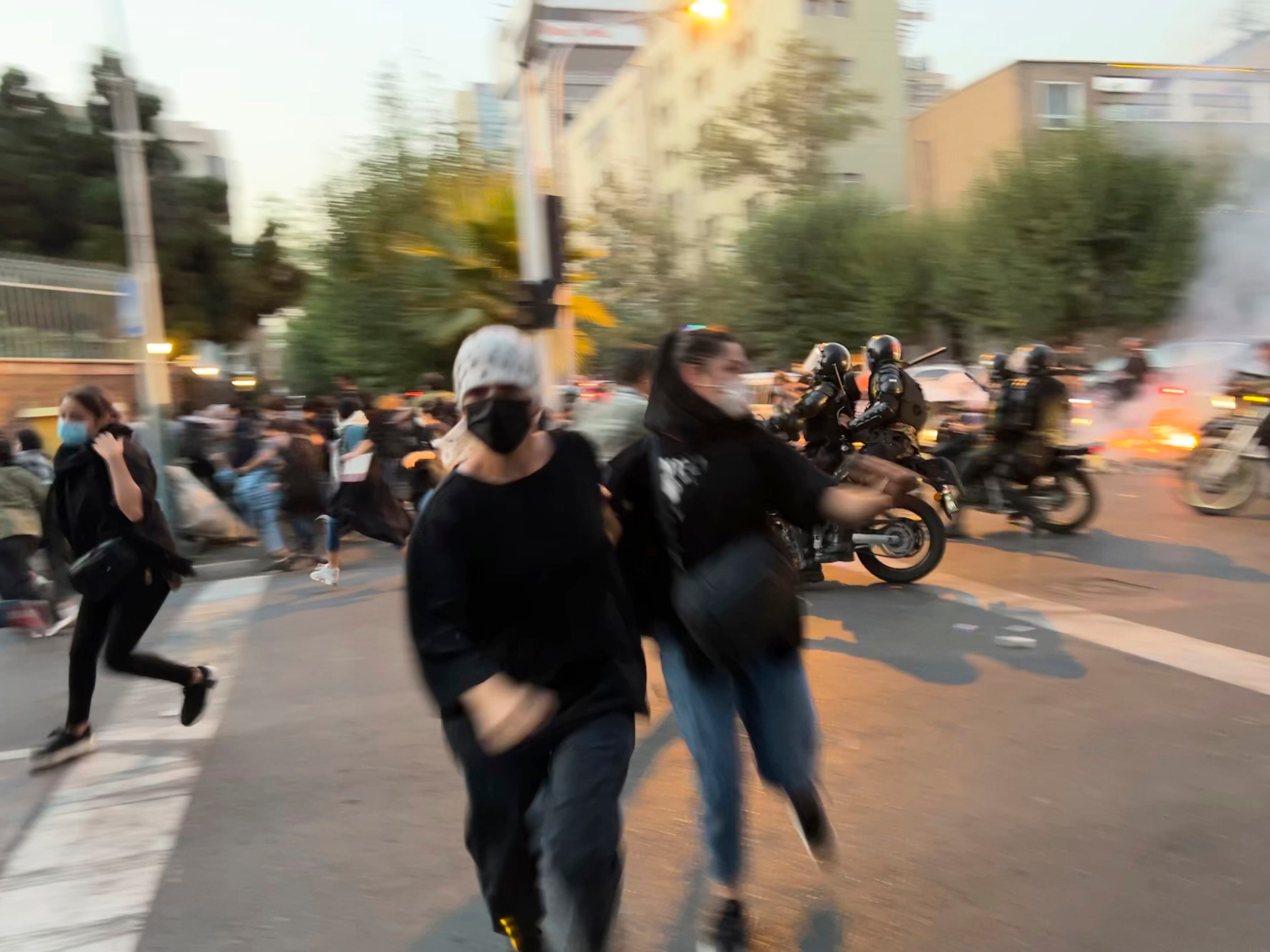 Two women flee from police during a protest in Tehran on September 20, 2022, following the death of Masha Amini.