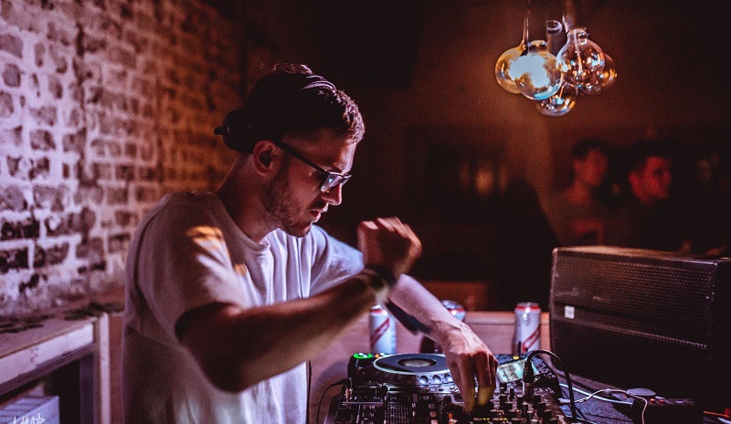 Deaf DJ Will Kirk spins tunes on his DJ deck with a brick wall and people in the background.