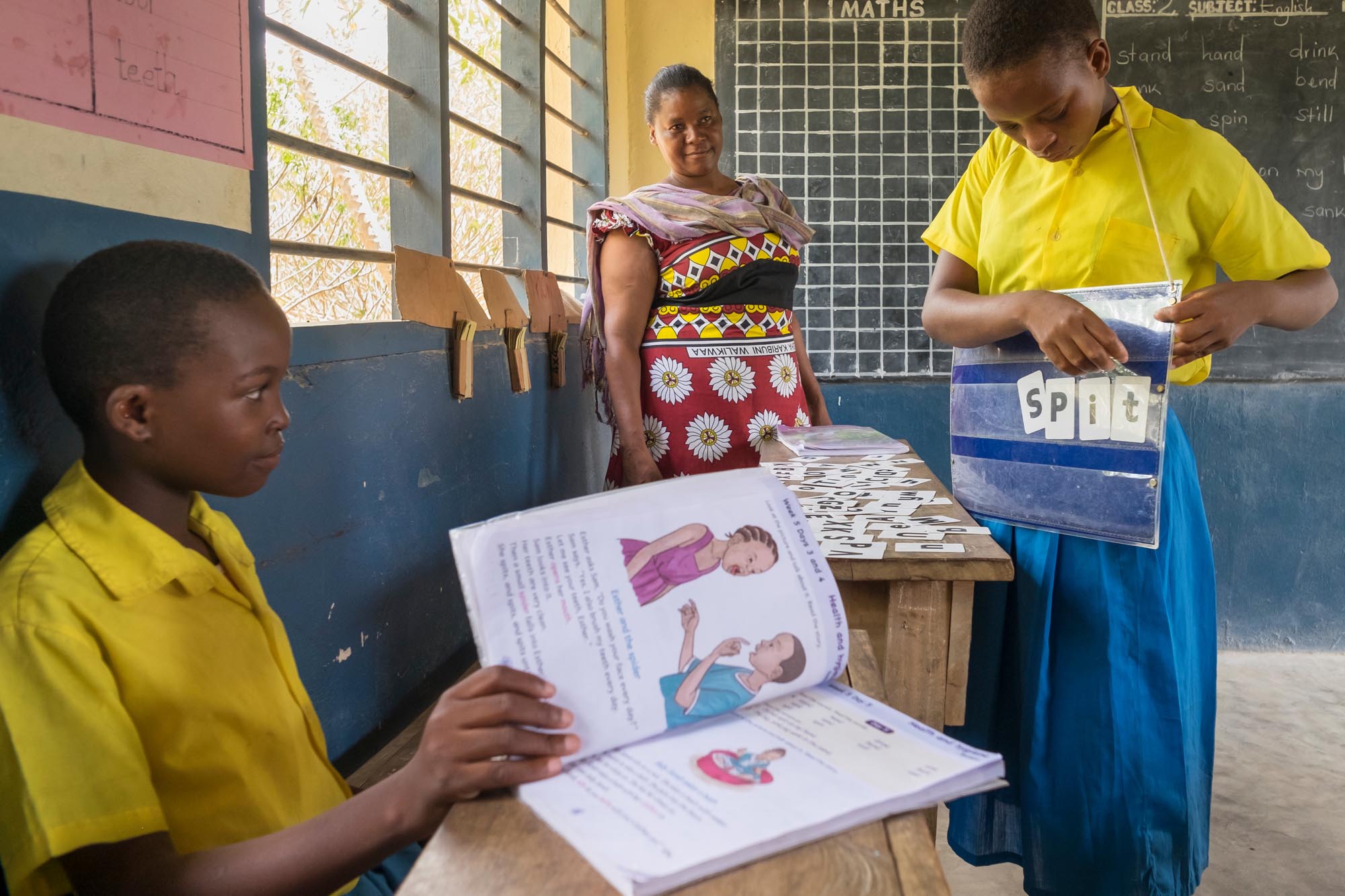 Two deaf children in Africa learning spellings in school while a teacher supervises