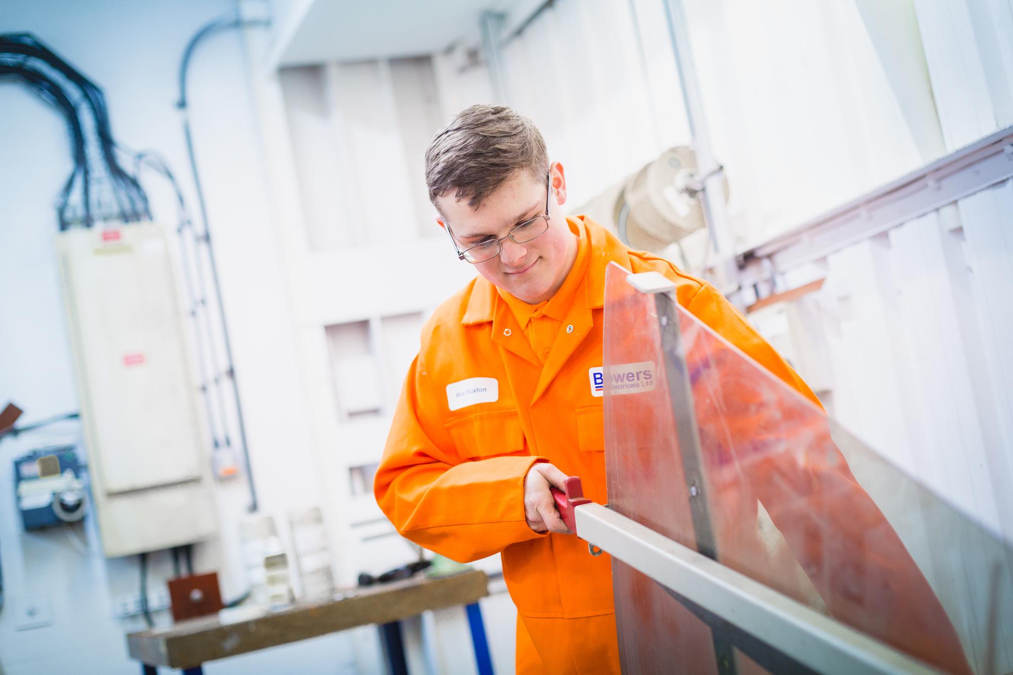A young man in an orange jumpsuit works at his engineering apprenticeship.