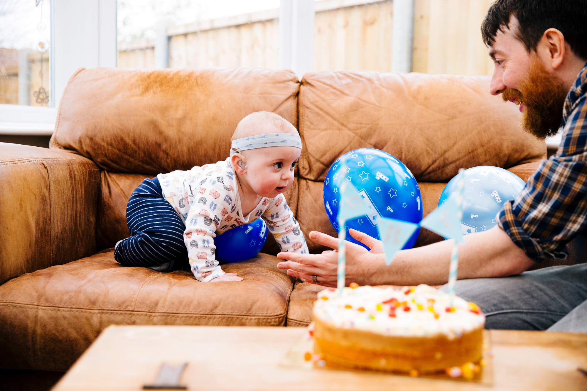 Dad and deaf toddler celebrating a birthday with cake and balloons