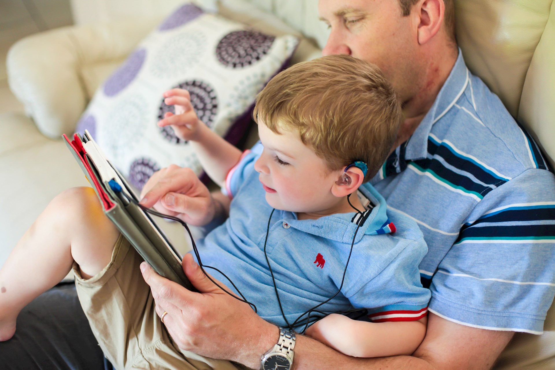 A deaf child with a hearing aid and a his dad watching a tablet together
