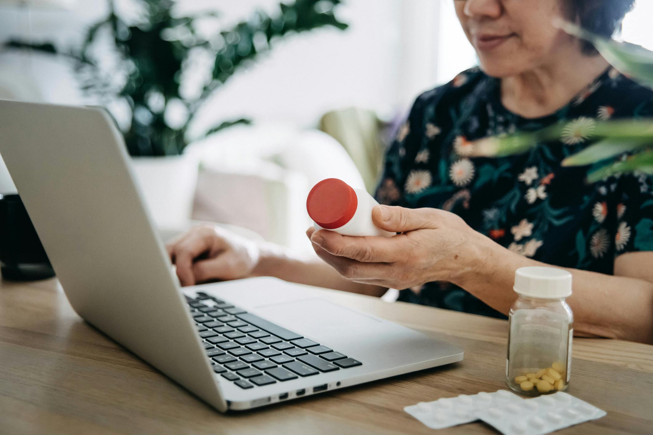 Senior Asian woman video conferencing with laptop to connect with her family doctor, consulting about medicine during self isolation at home in Covid-19 health crisis