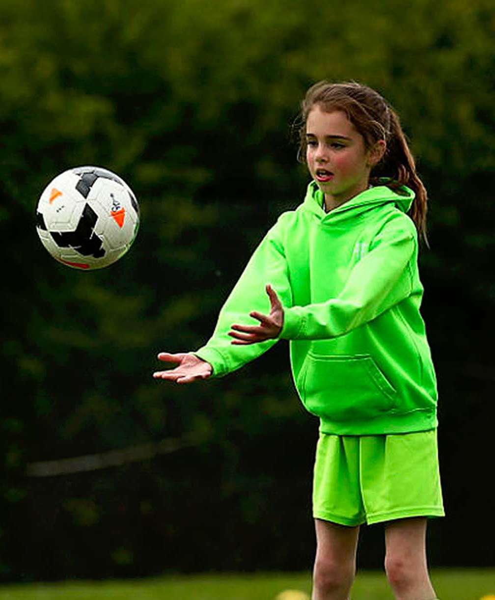 3 young girls wearing green hoodies and shorts throw a football to each other.