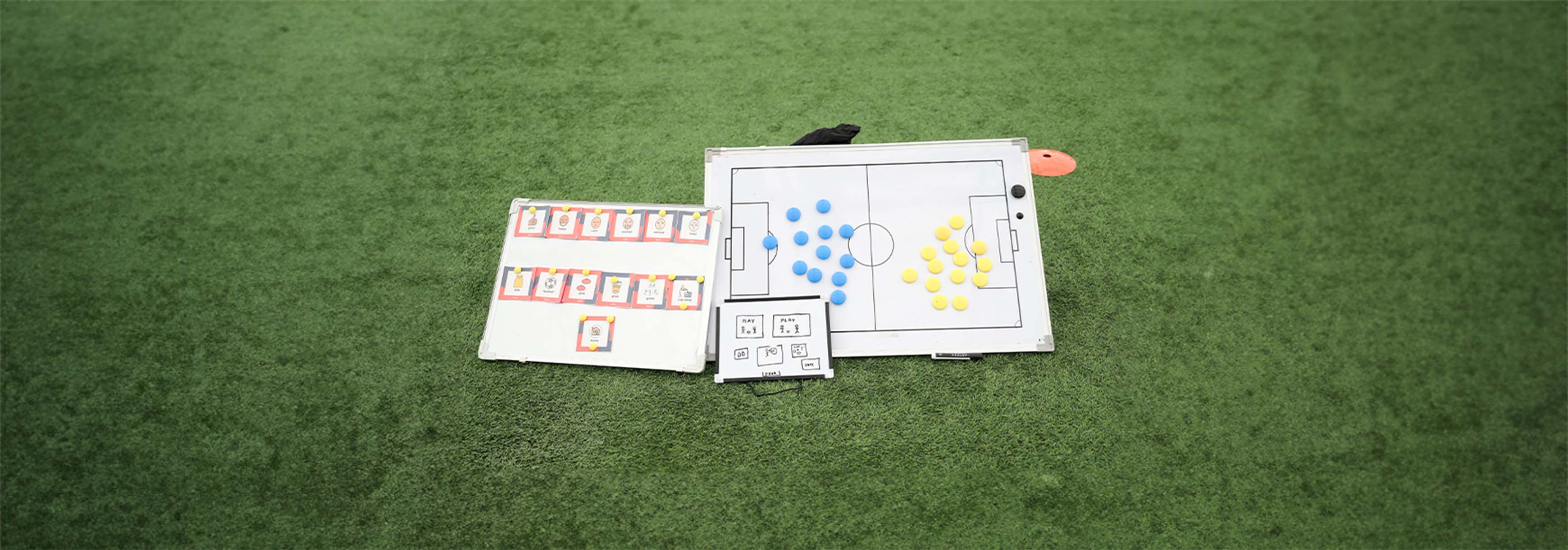 Three whiteboards placed on a 3G pitch. One shows flashcards, one shows the layout of the session and the other is used as a tactics board.