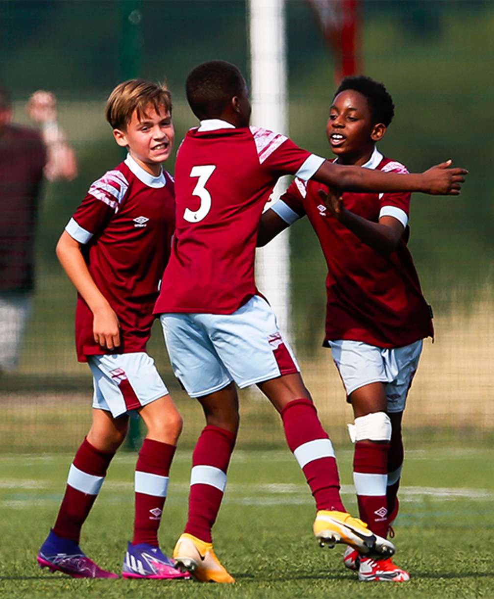 Six male football players celebrate on a pitch. They're around 12 years old.