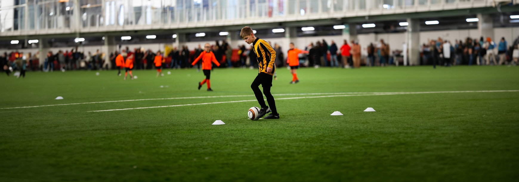 A young player controls the ball with the inside of his left foot and keeps it close to him during a match on an indoor 3G pitch.