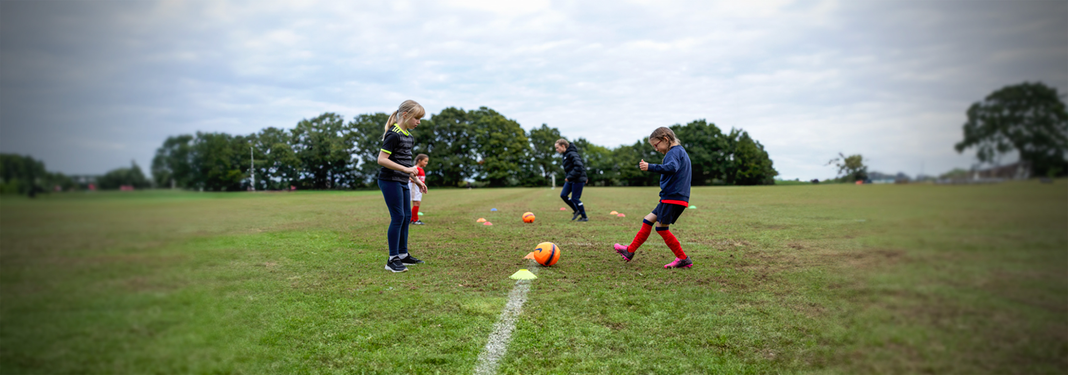 Two children face each other and kick a ball to each other between cones