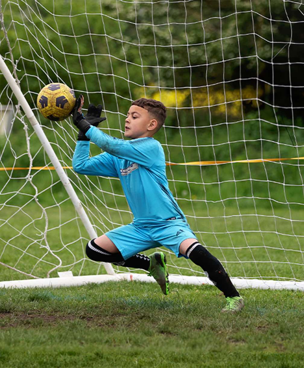 A young goalkeeper saves the ball, pushing a shot away with the palm of his left hand.