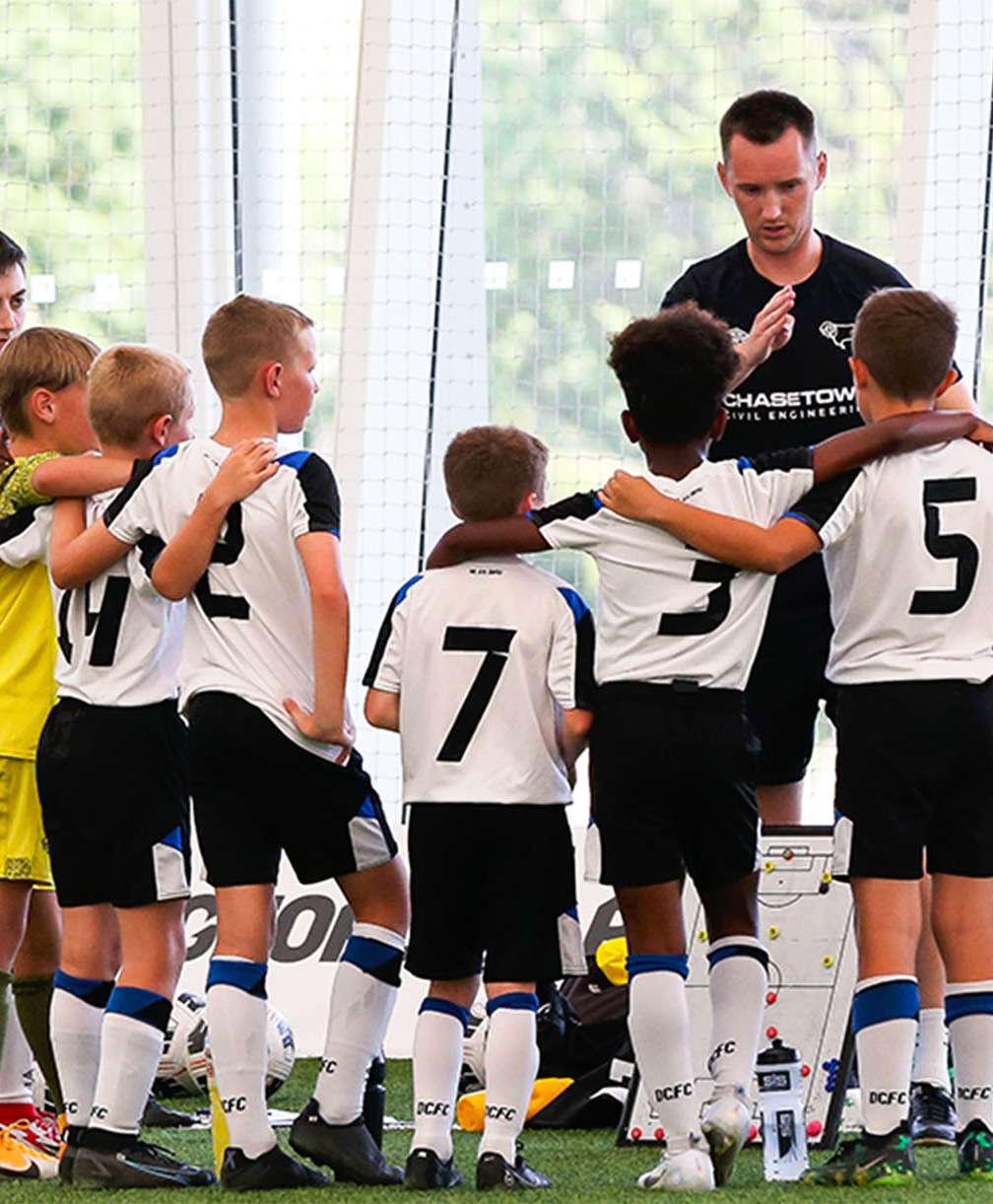 Players gather round their coach to listen to his instructions during a football tournament on the indoor 3G pitch at St. George's Park.
