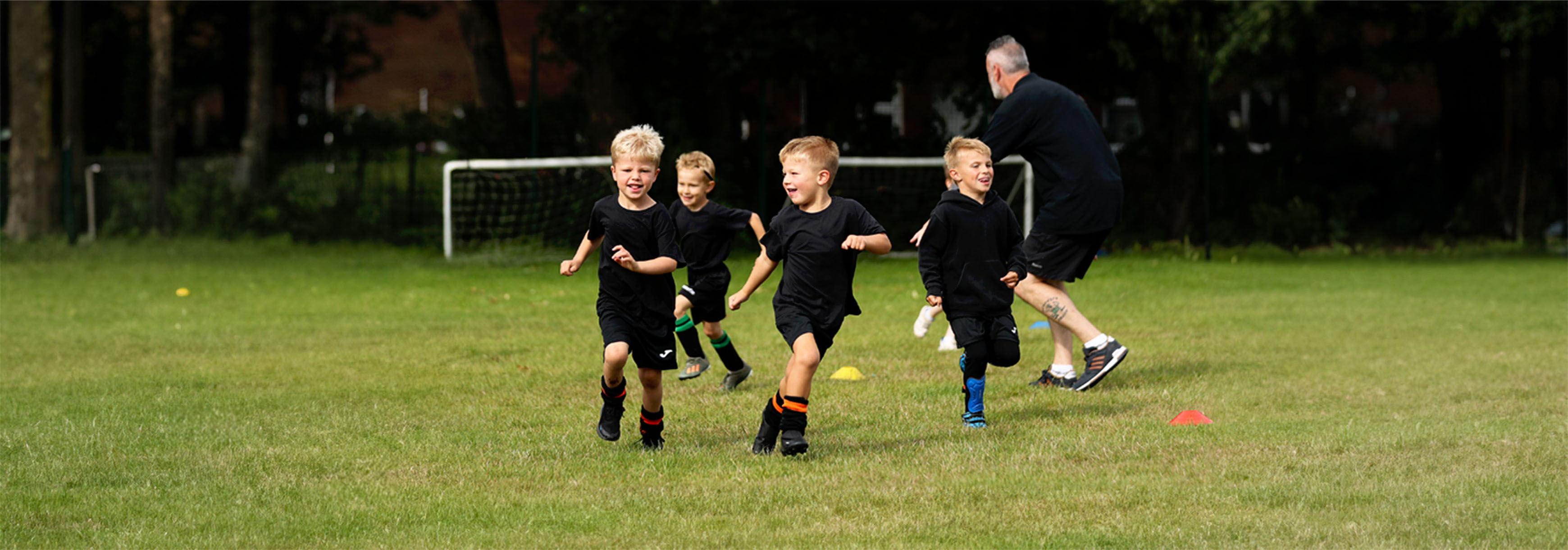 A group of young players aged four to six run around on a grass pitch playing tag.