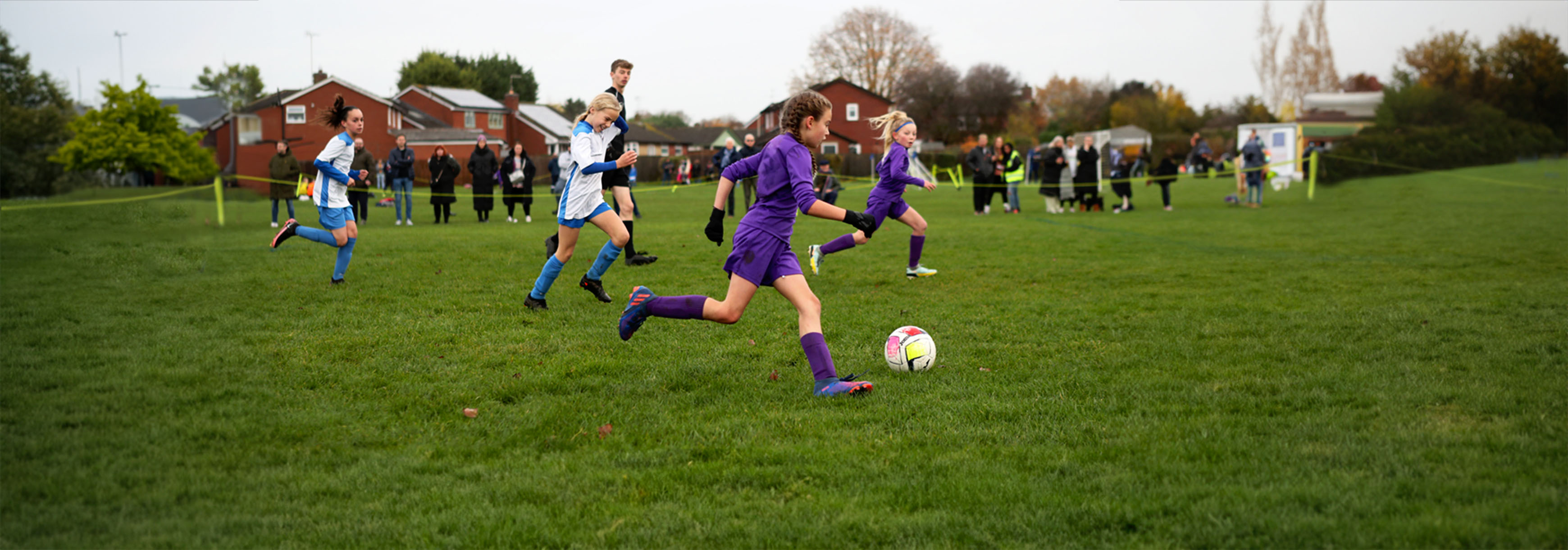 A young girl runs forward with the ball during a grassroots football match on a grass pitch.