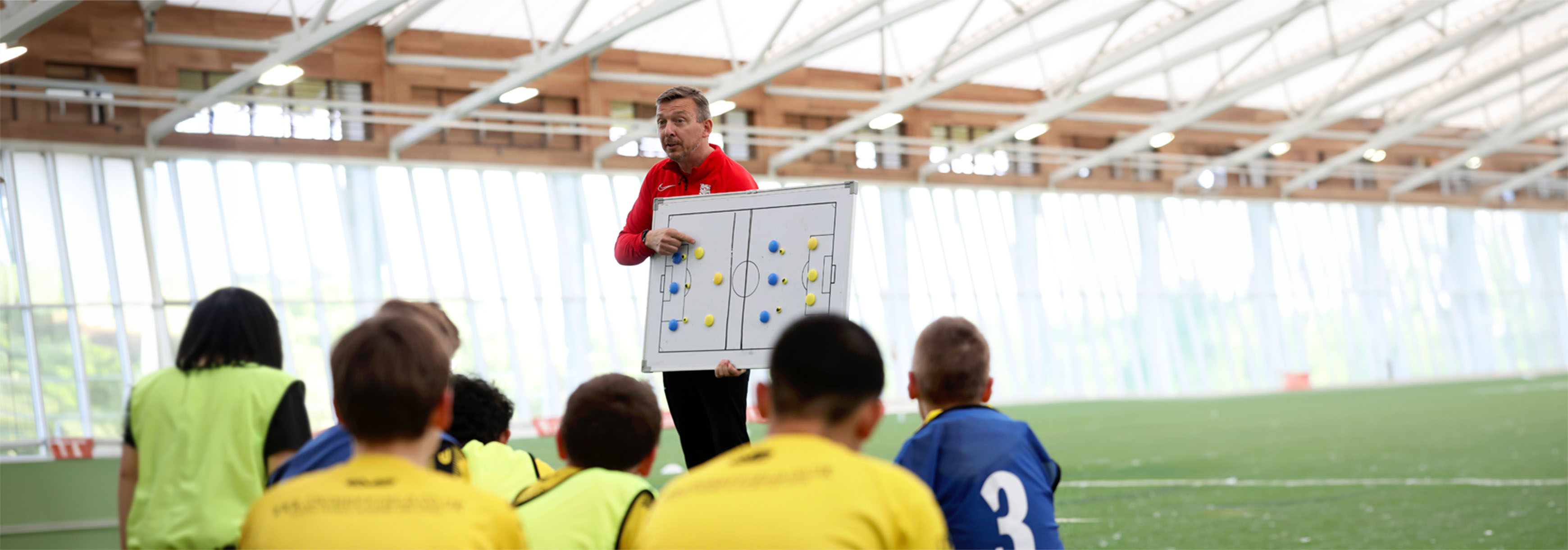 Coach points at board while players sit on the pitch