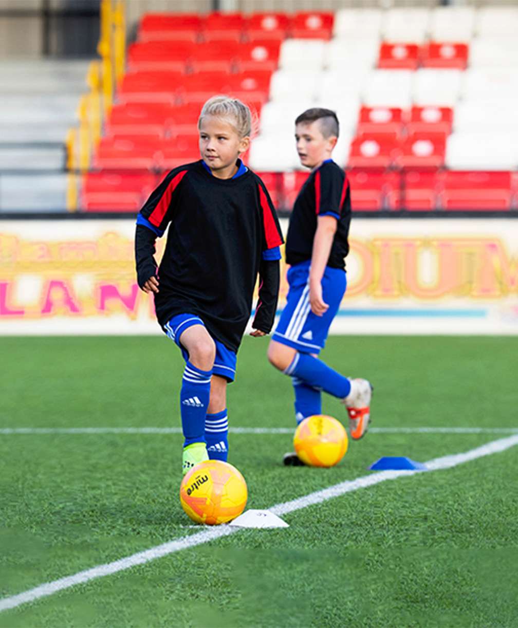 Three young players stand on the halfway line with a football at their feet during a training session.