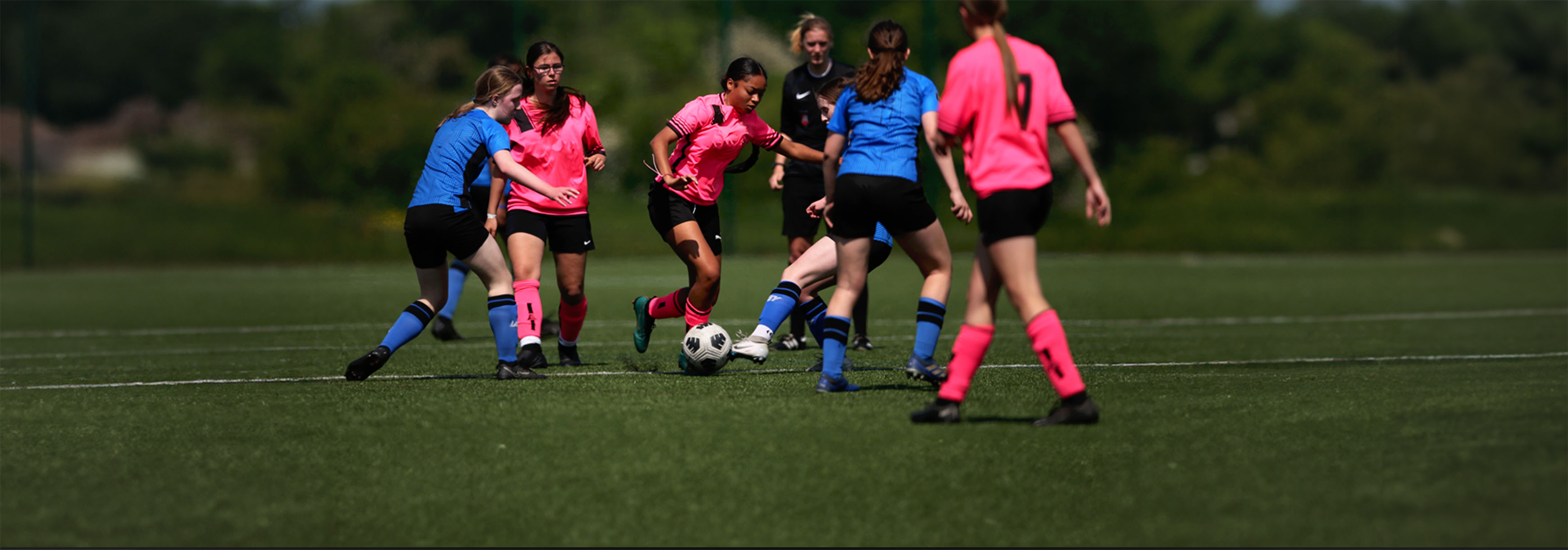 During a game, a player dribbles forward with the ball, with three opponents and two teammates in close proximity to her, and tries to avoid the challenge of a defender.