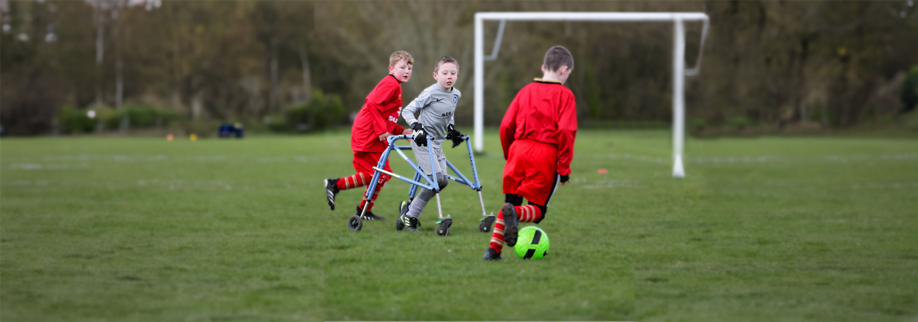 A child who is a frame user plays football on a grass pitch with two kids who aren't frame users.