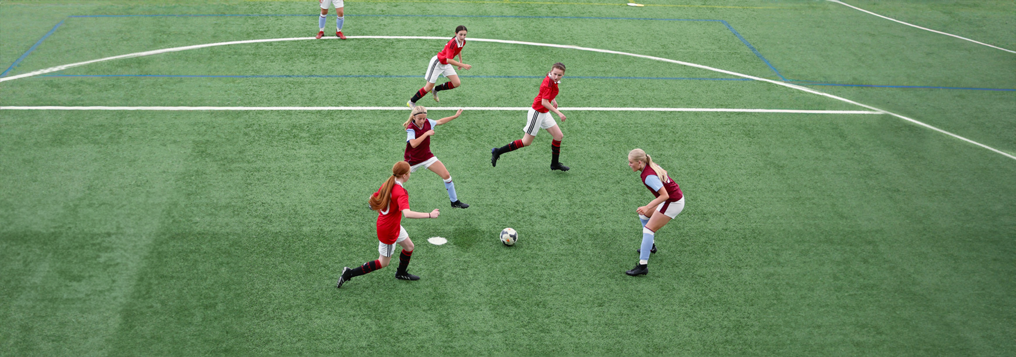 During a tournament on an indoor 3G pitch, a player passes the ball between two defenders to find one of her two teammates who are both running through.