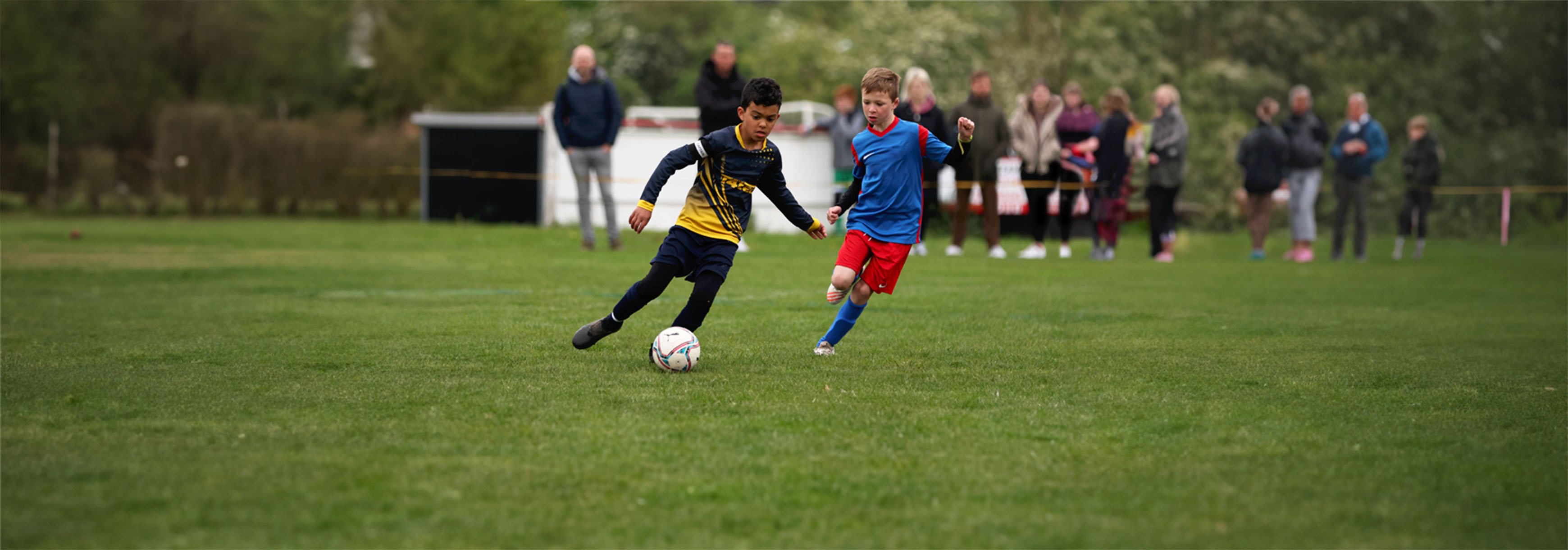A young player runs with the ball during a match, while his opponent is tracking back.
