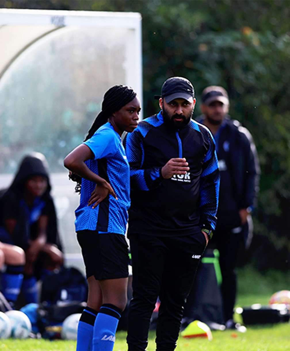 A player listens to her coach as he provides some instructions to her at the side of the pitch during a match.
