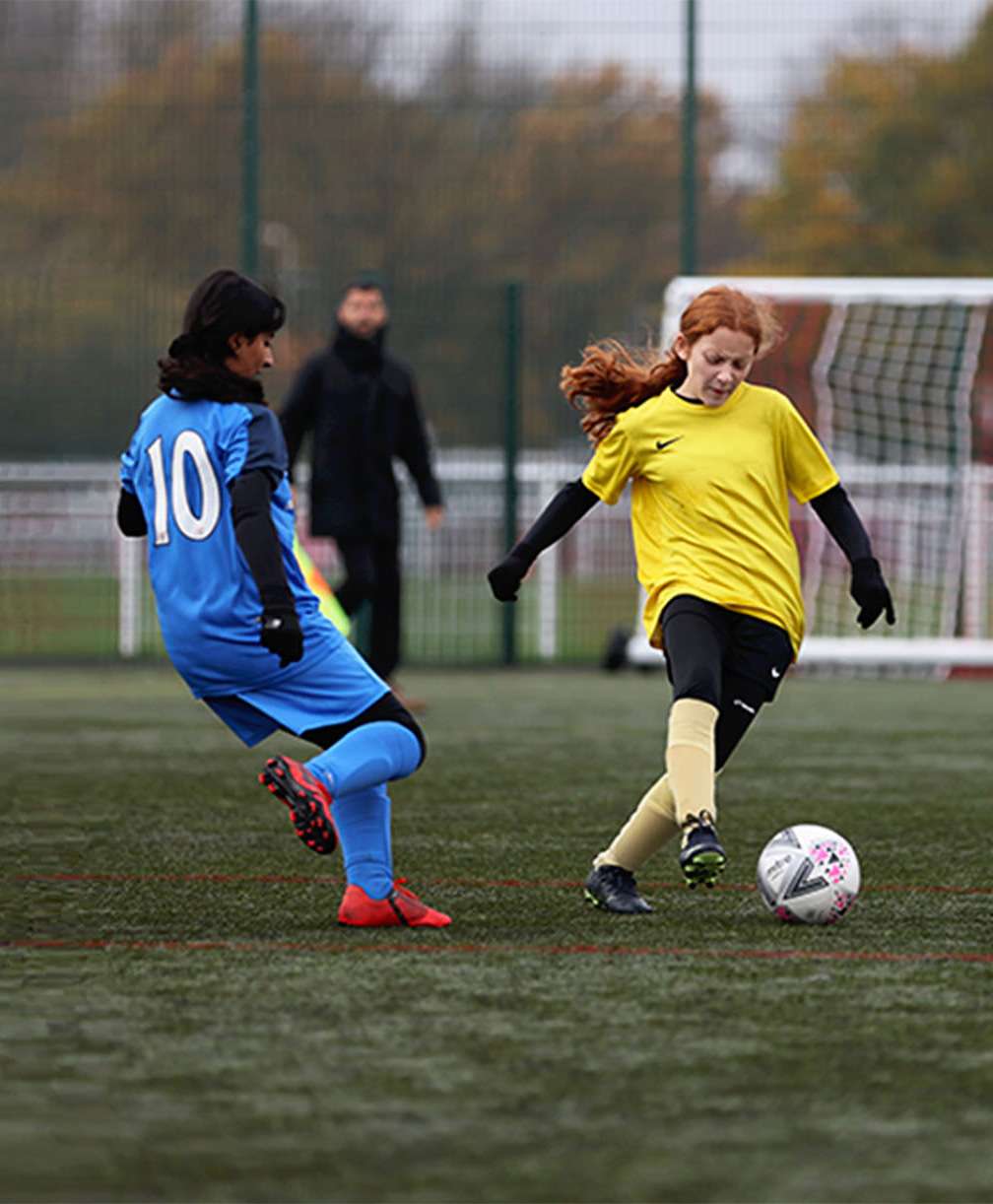 A young player, under pressure from an opponent, passes the ball with the inside of her foot during a match on a 3G pitch