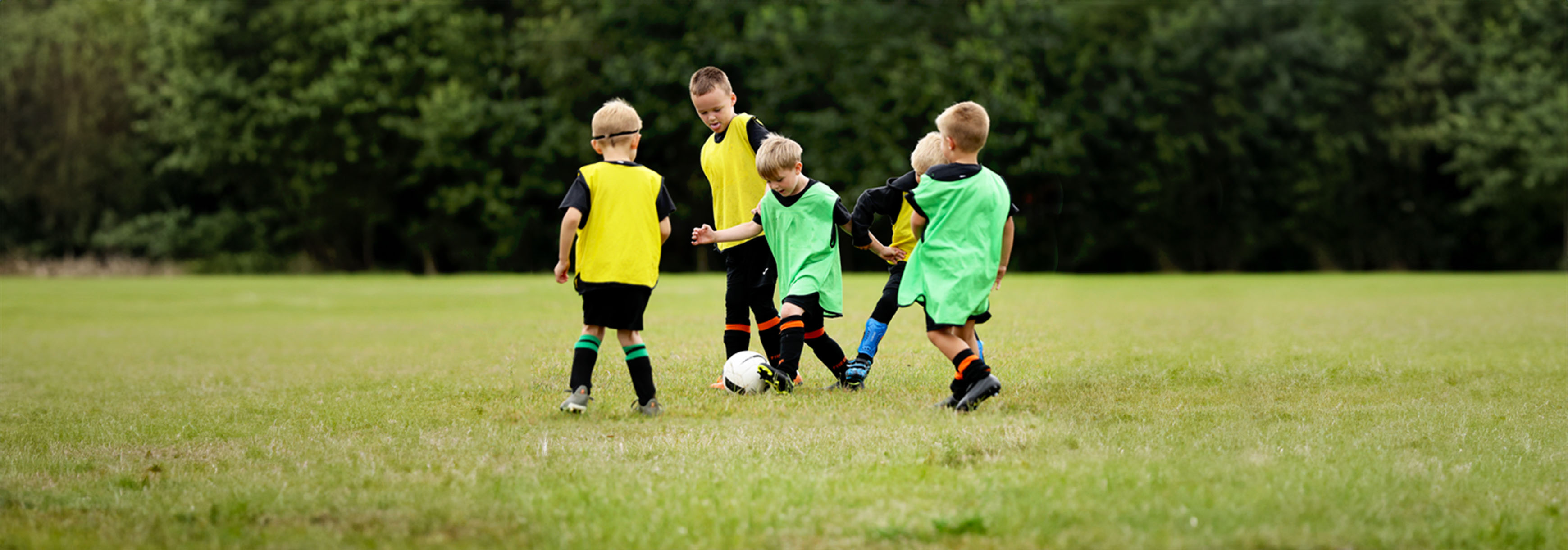 Five boys in the Play Phase take part in a small-sided game on a grass field.