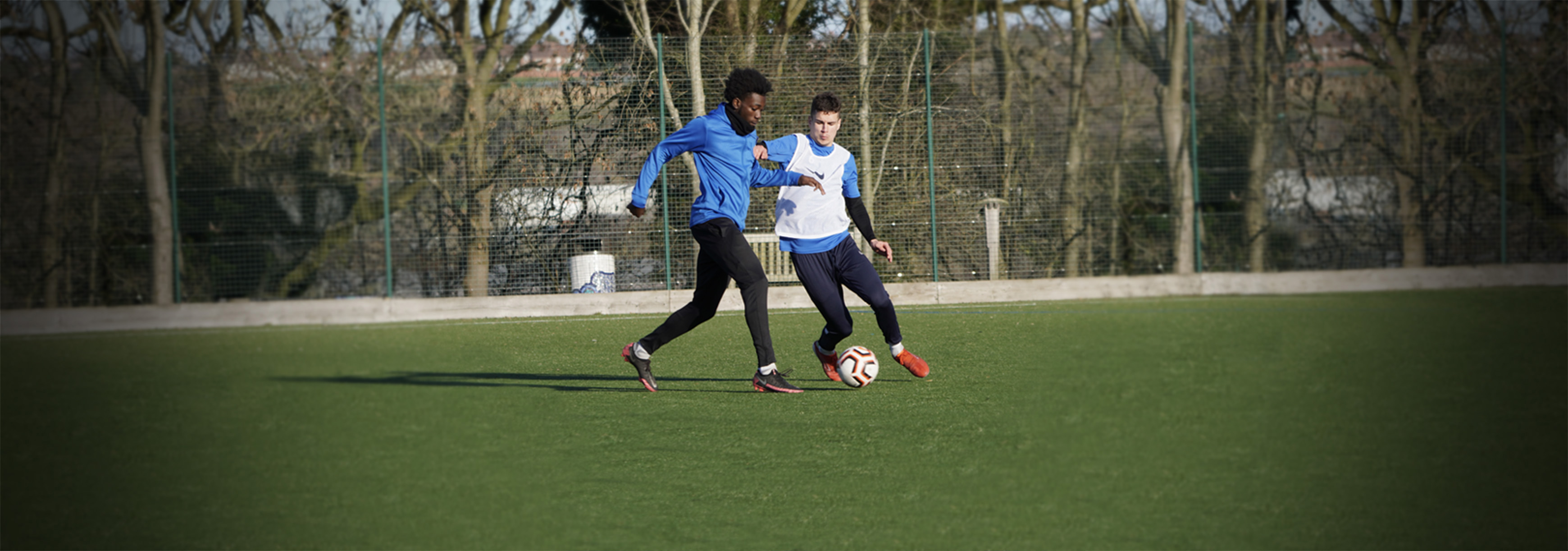 During a 1v1 practice, a player runs with the ball while his opponent looks to make a tackle.