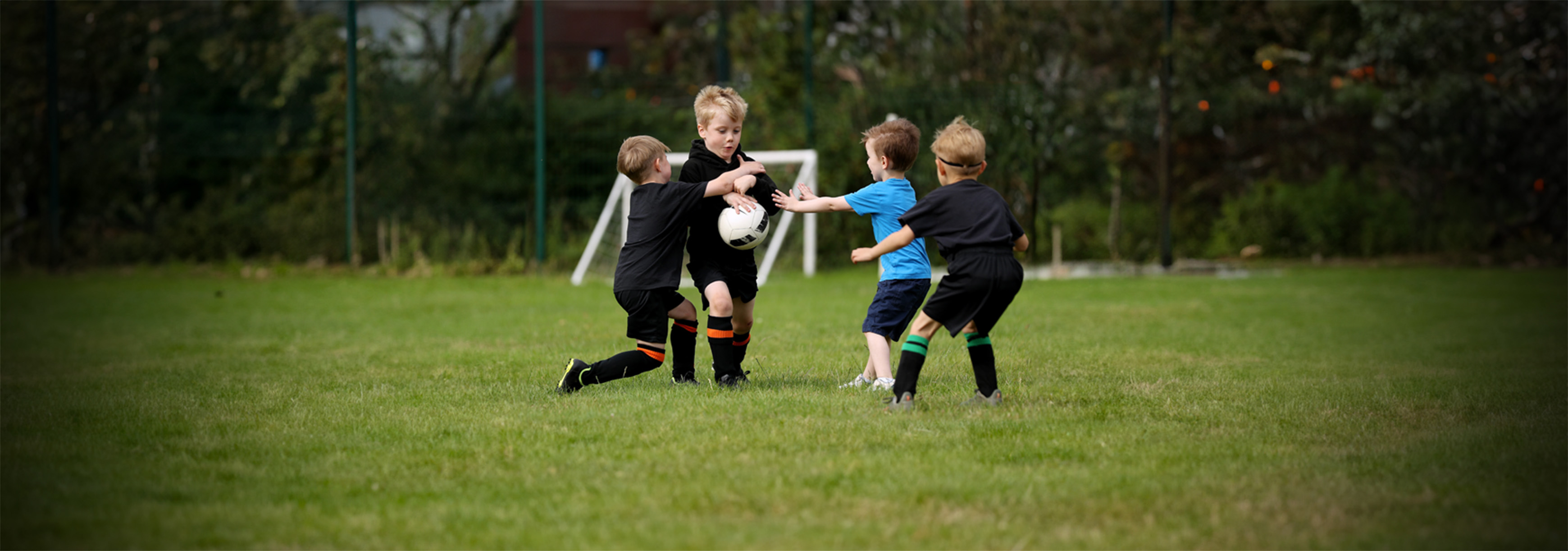 During a Play Phase session, a young boy runs with a ball in his hands while three others try to take it off him.