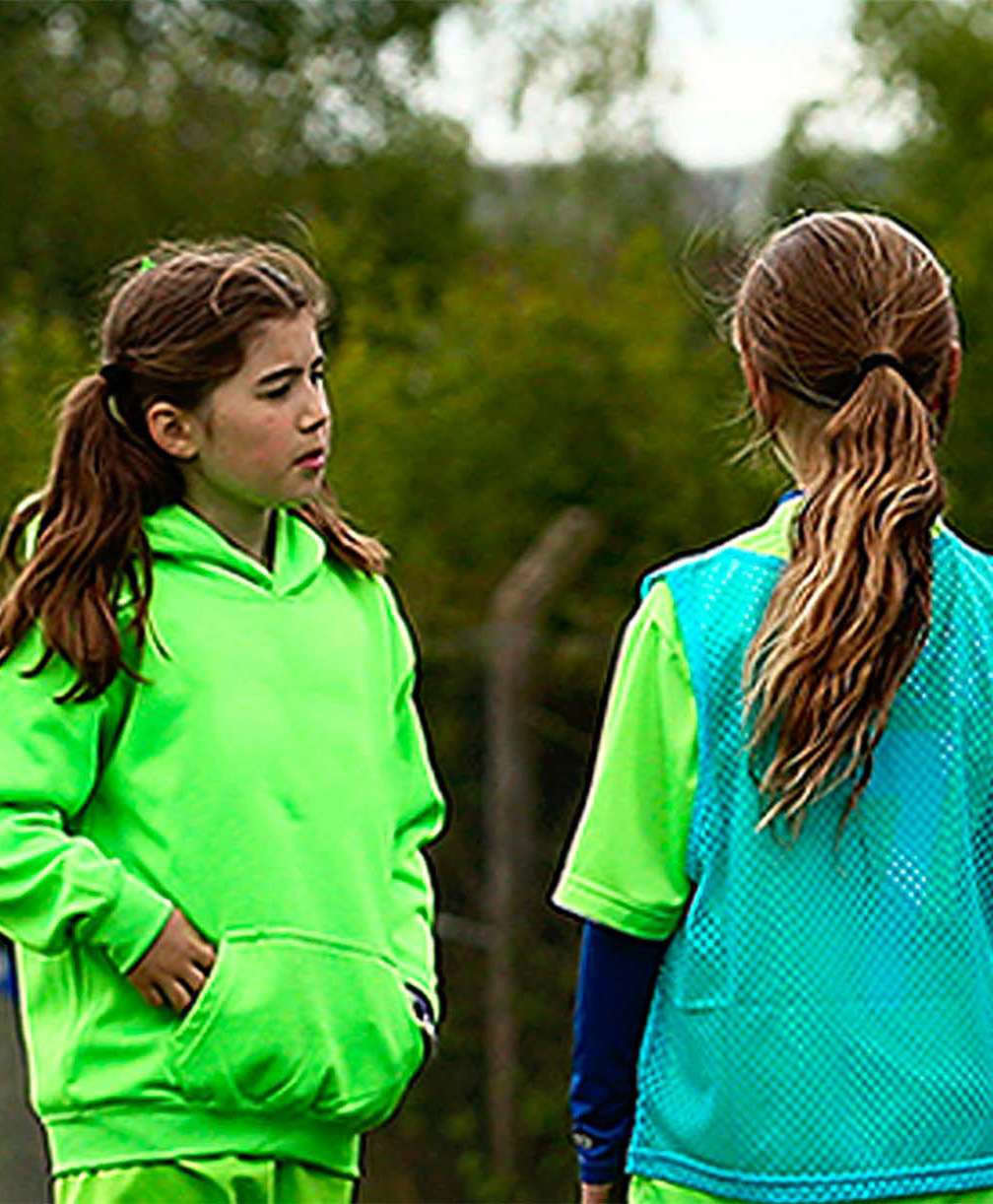 3 young female players wearing green kits look at their coach, a female wearing black.